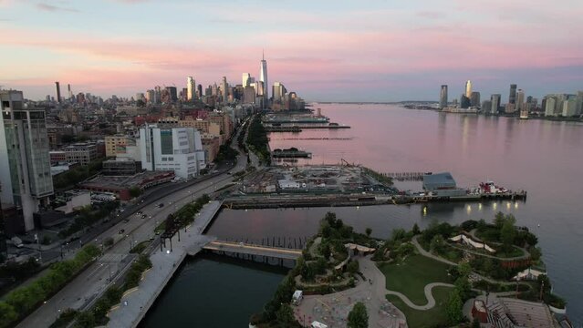 An aerial view of Manhattan from over the westside at sunrise. The drone camera dolly out and pan left slowly showing the Freedom Tower in the distance and a pink and blue sky