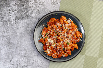 Red chicken pasta with herbs, tomatoes and cheese on a round plate on a dark gray background. Top view, flat lay