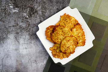 Rustic homemade Zucchini pancakes on a white square  plate on a dark background. Top view, flat lay