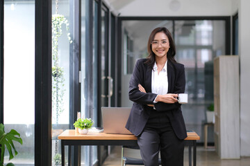 Confident Asian businesswoman standing with her arms crossed holding a coffee cup, smiling and looking at the camera.