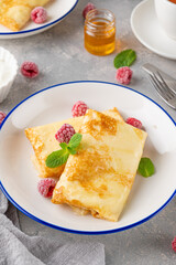 Traditional thin pancakes or crepes with cottage cheese, honey, sour cream and raspberries with cup of tea on a gray concrete background. Food for Maslenitsa. Copy space