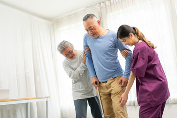 Asian young caregiver nurse and senior woman support senior older male to walk. Elderly wife taking...