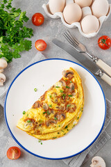 Omelet with fried mushrooms and fresh herbs in a plate on a concrete background. Delicious healthy breakfast. Top view. Copy space.