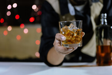 The bartender holds a glass of whiskey and ice to the male guest. service concept
