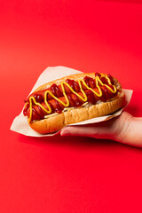 American Hotdog held in hand in a napkin against a red background