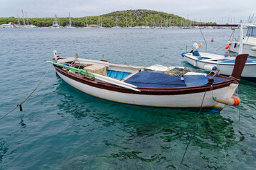 Fishing boat, white fishing boat for rowing in the beautiful blue crystal clear waters of the Croatian Mediterranean. In the background there is a marina and green mountains.