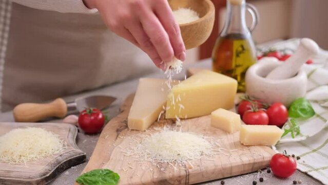 woman grates piece of parmesan hard cheese on a grater at domestic kitchen