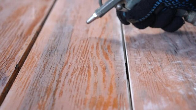 a man's hand blows dust off a wooden table, preparing for staining