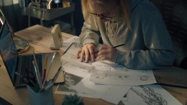 Young woman works on a storyboard in a home based design studio. A laptop and stationary jar on the table. Woman draws sketches as a roadmap for the video. Pre-production.
