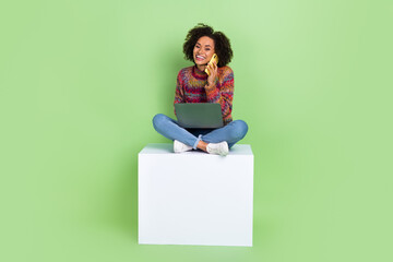 Full size portrait of pretty cheerful girl sit podium speak telephone use netbook isolated on green color background