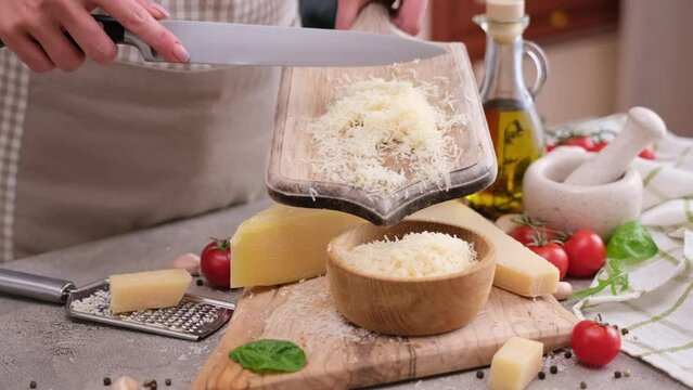 Woman pours grated parmesan cheese from wooden board into bowl