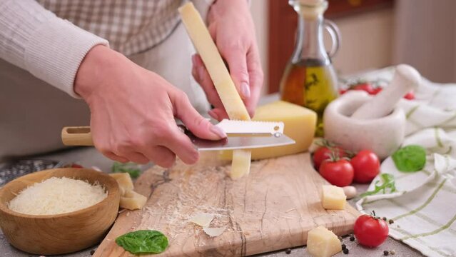 woman slicing piece of parmesan hard cheese at domestic kitchen