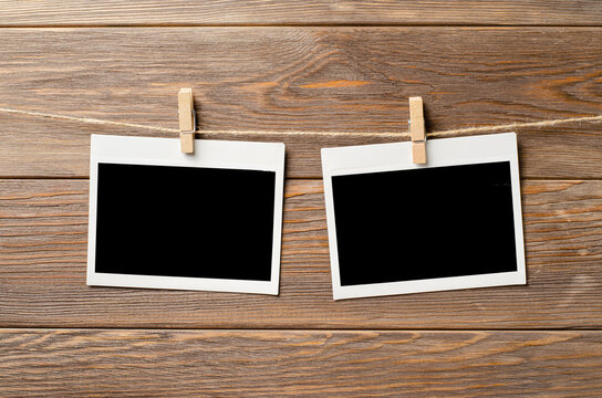Empty photos are hanging on a rope. A design element. Brown wooden background. Copy space.