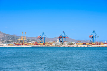 Landscape of the port of Malaga with cranes, containers, blue sky and mountains.