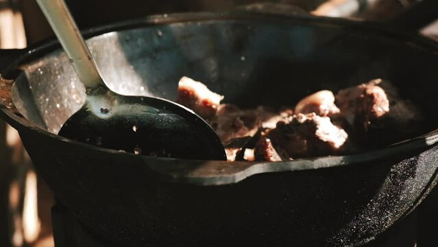 A man roasts meat in a cauldron on an open fire.Close up,slow motion.