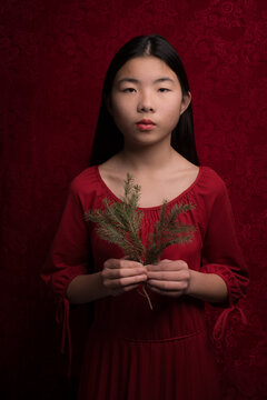 Asian girl in red dress holding christmas tree branch in studio portrait