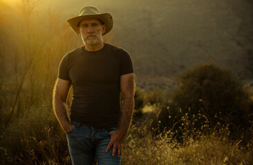 Portrait of adult man in cowboy hat standing in field during sunset