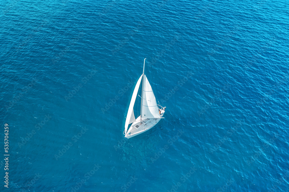 Wall mural Aerial view of beautiful white sailboat sailing in the blue sea on a sunny day. Peaceful landscape with yacht. Top view of boat