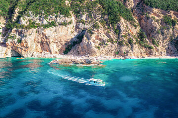 Top view of beautiful seascape with rock, blue sea, sandy beach and white boat near the coastline in the day. Islands of Sardinia in Italy, aerial drone shot