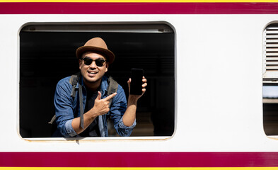 Young asian man travel by train. Sticking his head outta the train window showing smartphone....
