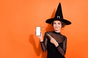 Photo of pretty sorcerer person direct finger empty space telephone screen isolated on orange color background