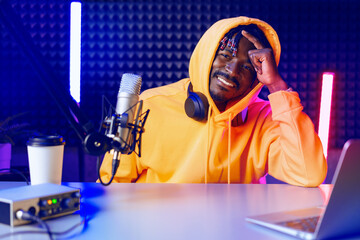 African radio host sitting at desk recording in studio with microphone and laptop