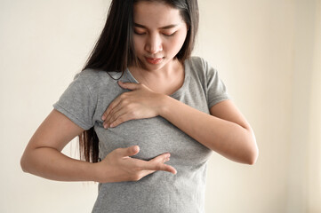 Young Asian woman pressing touching her chest for checking lady breast cancer symptom diagnosis...