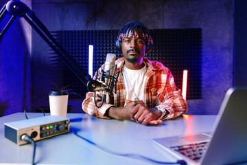 African radio host sitting at desk recording in studio with microphone and laptop