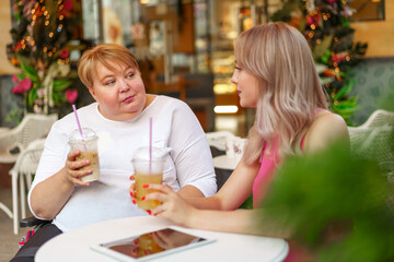 Young daughter and her mother in wheelchair sitting at the table in cafe with drinks and having fun