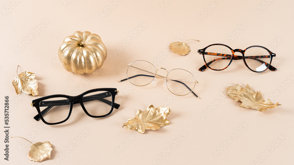 Wall mural Eyewear fashion. Trendy glasses in plastic and matallic frame on a beige background with golden leaves. Trendy glasses still life, minimalism. Fall fashionable accessories. Optic store discount, sale.