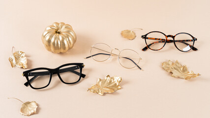 Eyewear fashion. Trendy glasses in plastic and matallic frame on a beige background with golden leaves. Trendy glasses still life, minimalism. Fall fashionable accessories. Optic store discount, sale.
