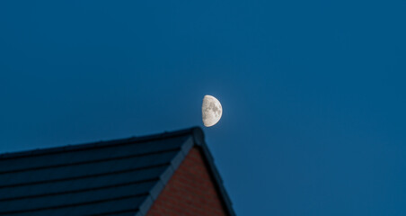 Fototapeta na wymiar Half moon shining above the building rooftop 