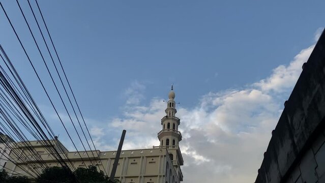 Mosque minaret tower symbols of Islam during azan time, tilt down to road full of traffic, day