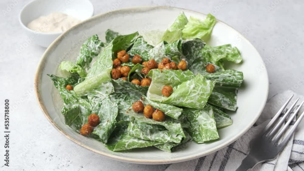 Poster Vegan caesar salad with fried spicy chickpeas in a gray bowl.