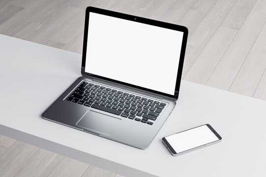Close up of empty white laptop and smartphone on light desktop, mock up place on screen, wooden parquet flooring background. Top view. 3D Rendering.