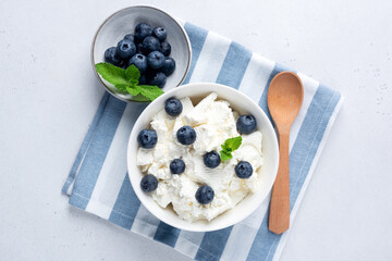 Cottage cheese, quark or curd in bowl served with blueberries on blue and white striped linen textile. Rich in calcium and protein dairy product, table top view