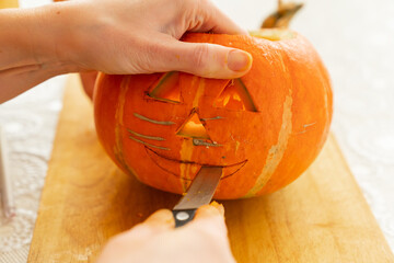 hands carves a lantern out of a pumpkin for halloween.