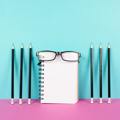 Empty notebook with a pencils and eyeglasses on a pink and blue background, brainstorming for new...