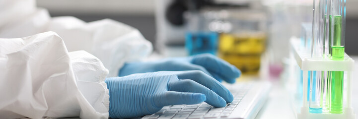 Hands of scientist in gloves works on keyboard in laboratory closeup