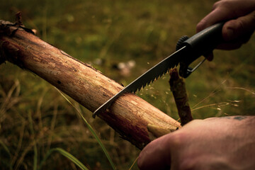 a man cutting wood with a saw in the forest, preparing a fire.