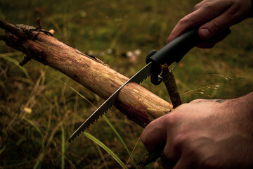 a man cutting wood with a saw in the forest, preparing a fire.