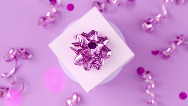 gift box with a bow rotates on a pink background, sparkles of festive confetti are pouring from above