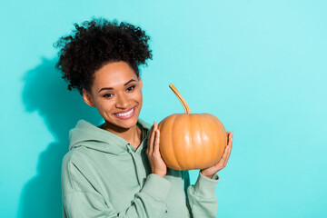 Portrait of cheerful pretty lady arms hold pumpkin beaming smile isolated on vibrant aquamarine...