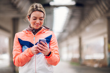 Young woman taking a break from jogging outside and using smartphone