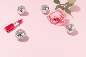 Romantic composition of pink rose flower, red lipstick and shiny disco balls on bright pink...