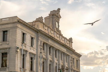 The chamber of commerce old Consular Palace with a French written engraving and a clock on the roof. Flying bird, cloudy sky with golden hour sunlight in the background.