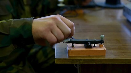 Close-up of the hand of a military radio operator transmitting data via telegraph using Morse code. The telegraph key or Morse key in action.