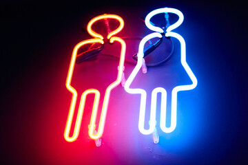  Illuminated sign of man and woman in red and blue colors. Neon images of boy and girl
