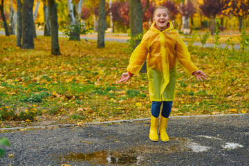 A happy girl in a yellow raincoat and rubber boots on an autumn walk.