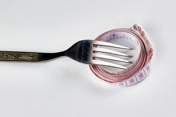 iron fork rewound with measuring tape on a white background concept diet